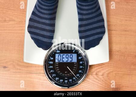 Personne se pesant sur une échelle numérique et analogique blanche avec des chaussettes rayées sur un plancher en bois. Vue de dessus. Banque D'Images