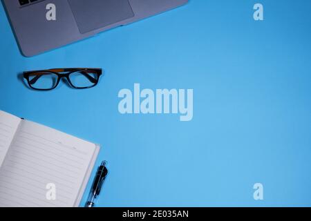 Concept de bureau, vue de dessus de l'espace de travail avec ordinateur, lunettes et ordinateur portable sur fond bleu Banque D'Images