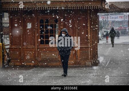 Srinagar, Inde. 29 décembre 2020. Un homme porte un masque facial lorsqu'il marche à travers un pont à pied pendant une chute de neige fraîche à Srinagar.une chute de neige fraîche a été enregistrée dans certaines parties de la vallée du Cachemire, y compris la capitale estivale, Srinagar, menant à la fermeture de la route nationale Srinagar-Jammu, ont déclaré les responsables. Crédit : SOPA Images Limited/Alamy Live News Banque D'Images