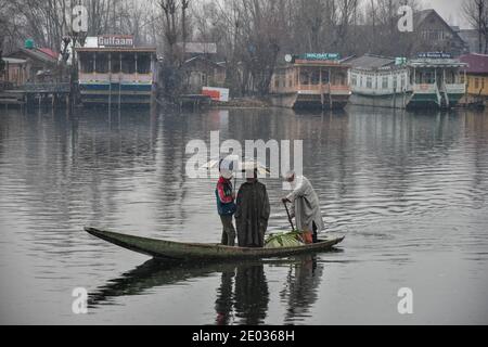 Srinagar, Inde. 29 décembre 2020. Un homme fait des ferries de passagers dans son bateau pendant les chutes de neige fraîches à Srinagar.des chutes de neige fraîches ont été enregistrées dans certaines parties de la vallée du Cachemire, y compris la capitale estivale, Srinagar, conduisant à la fermeture de la route nationale Srinagar-Jammu, ont déclaré les responsables. Crédit : SOPA Images Limited/Alamy Live News Banque D'Images