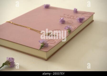 Agenda rose et pendentif en métal sur la table entourée de fleurs Banque D'Images
