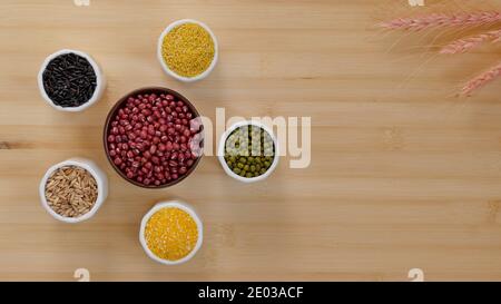 Vue de dessus des haricots et des grains sur une table en bois. Les gruau de maïs, les haricots mungs, le riz noir, les baies de blé et le millet dans cinq tasses de céramique blanche entourent adzuki Banque D'Images