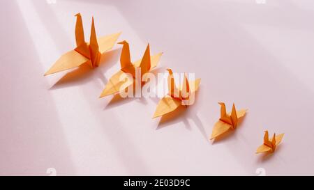 Grue orange origami sur fond rose, de petite à grande dans une barre oblique, concept de croissance Banque D'Images