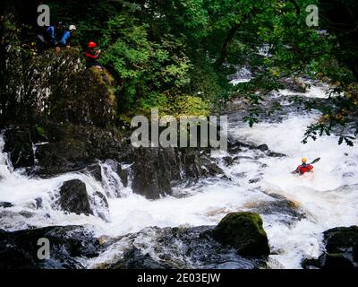 Canoéiste qui navigue sur la chute d'eau rocheuse, Swallow Falls, avec d'autres membres de l'équipe qui s'intéressent. Betws-y-Coed, Conwy, pays de Galles du Nord, Royaume-Uni Banque D'Images