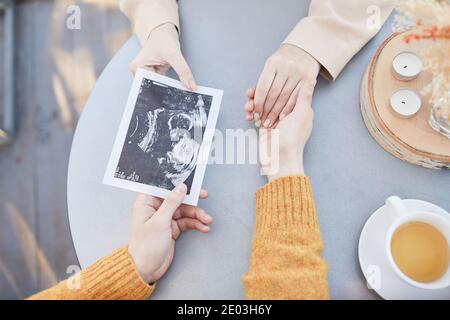 Gros plan d'un couple assis à la table avec une table à thé mains et regarder la première échographie de leur bébé Banque D'Images