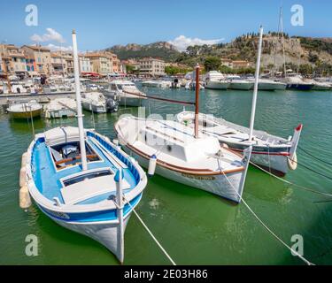 Trois petits voiliers amarrés dans le port de cassis en Provence, en France, par une journée ensoleillée avec le front de mer et le château en arrière-plan Banque D'Images