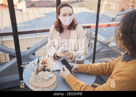 Jeune femme en masque parlant au jeune homme pendant qu'ils assis à la table pendant la réunion dans le restaurant Banque D'Images