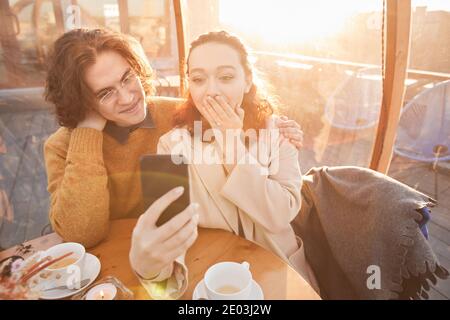 De vieux amis regardant des photos sur leur téléphone mobile et souriant lors de leur réunion au café Banque D'Images
