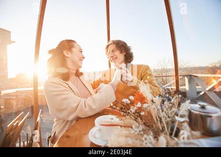 Un couple heureux se tenant les mains et souriant les uns envers les autres a une date dans un endroit magnifique dans le restaurant Banque D'Images