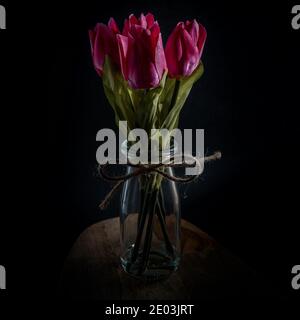 Bouquet de fleurs de tulipe rose dans une bouteille en verre isolée sur fond noir. Banque D'Images