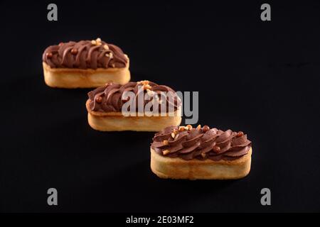 Trois desserts maison faits maison avec biscuits isolés sur fond noir. Biscuits sablés avec garniture mascarpone au chocolat brun fouetté. Concept de bonbons, industrie alimentaire. Banque D'Images