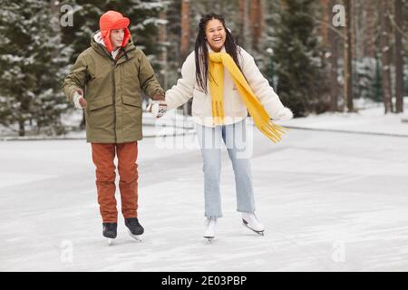 Couple heureux tenant les mains patiner ensemble dans la forêt d'hiver Banque D'Images