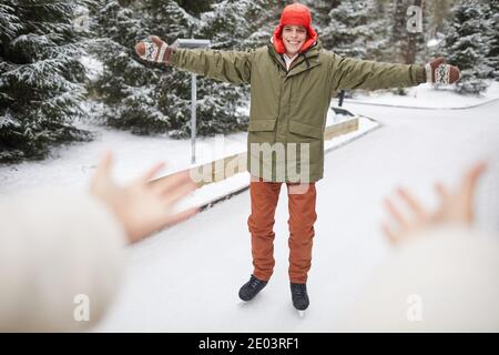 Joyeux jeune homme dans des vêtements chauds patinage sur la patinoire en hiver dans le parc Banque D'Images