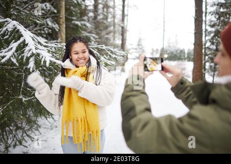 Une femme heureuse souriant et posant à la caméra pendant que l'homme fait photo sur téléphone mobile dans la forêt Banque D'Images