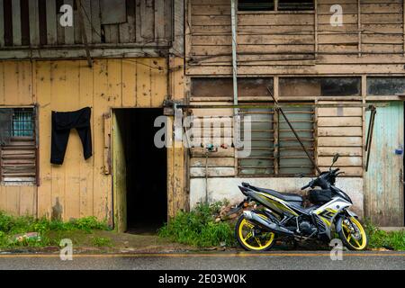 Village asiatique. Une ancienne maison en bois près de laquelle se tient une moto moderne. Les vêtements sèchent sur une corde à proximité. Banque D'Images