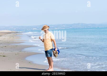 Homme debout sur la mer tout en tenant des chaussures et en observant un coque Banque D'Images
