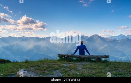 Personne de derrière assis sur un banc en bois regardant vue panoramique avec montagnes à l'horizon Banque D'Images