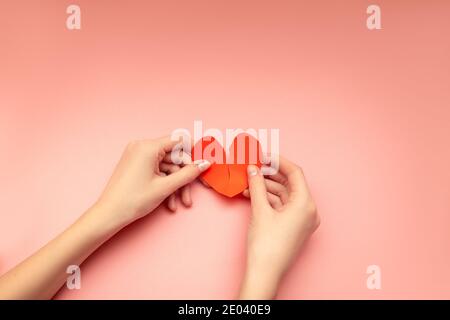 Coeur brisé dans les mains des femmes, débordant de Valentin sur fond rose. Concept de déception, séparation, séparation Banque D'Images