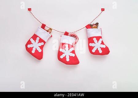 Trois chaussettes en tissu rouge et blanc avec des cadeaux de Noël sur la corde sur fond blanc. Vue de dessus. Banque D'Images