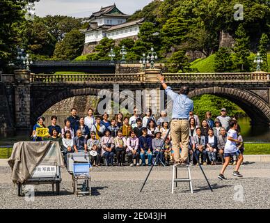 Un photographe lève la main pour attirer l'attention d'un grand groupe de touristes devant le pont Seimon Ishibashi au palais impérial de Chiyoda, à Tokyo. Le pont de pierre, connu sous le nom de Nijubashi, date de 1889. La tour de guet historique Fushimi-yagura se dresse derrière lui. Banque D'Images