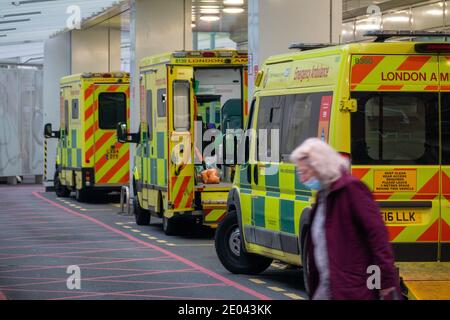 Baie d'ambulance pleine à l'hôpital University College alors que les hôpitaux de Londres luttent contre les cas de coronavirus. Une vieille dame traverse la route devant les ambulances portant un masque de visage tandis que les ambulanciers paramédicaux nettoient une ambulance avec ses portes ouvertes. Londres a eu du mal à faire face à la nouvelle souche de Covid19 et a déclaré un incident majeur. Service d'ambulance de Londres prenant en main plus de 999 000 appels d'urgence que jamais. University College London Hospitals NHS Foundation Trust. Banque D'Images