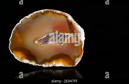 Couper la pierre gemeine avec des cristaux de quartz dans geode sur fond noir. Minéral cristallin clair et violet à l'intérieur de la cavité d'un joyau rouge-jaune-brun. Banque D'Images