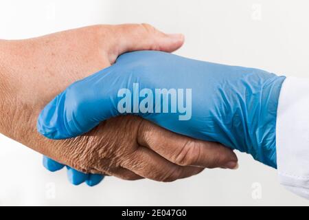 Aide main d'un professionnel de la santé tenant la vieille paume froissée sur fond blanc. Détail de la poignée de main sécuritaire du médecin dans un gant bleu et un patient âgé. Banque D'Images