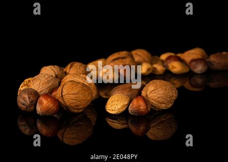 Noix de Grenoble, pacanes, noisettes, amandes en carapace sur une surface réfléchissante noire Banque D'Images