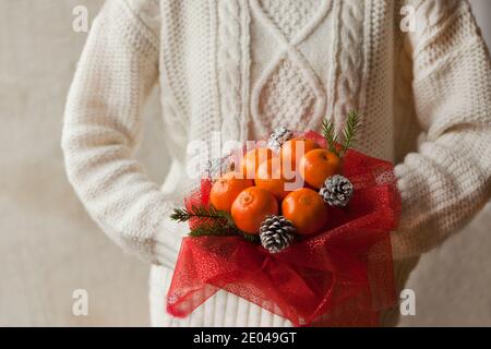 Femme mains en chandail blanc tenant un bouquet de mandarins et branches d'arbre de Noël. Bouquet de fruits comestibles du nouvel an. Cadeau de Noël. Utile Banque D'Images