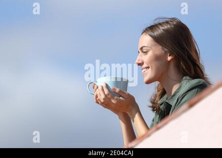 Vue latérale d'une femme heureuse contemplant des vues de balcon de l'appartement pour boire du café Banque D'Images