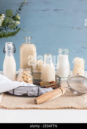 Types de laits alternatifs en bouteilles sur une nappe rustique. Des pots de cristal pleins de graines, céréales et noix sont à côté d'eux. Vue verticale. Banque D'Images