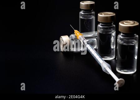 Vaccins, toxine botulinique et ampoules d'insuline concept thème avec des flacons en verre avec liquide clair à côté d'une seringue et une aiguille hypodermique isolée sur b Banque D'Images