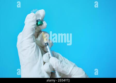 Médecin asiatique féminin avec des gants en caoutchouc blanc et un masque chirurgical dans une clinique, en insérant une aiguille et une seringue sur une bouteille en verre transparent de vaccin à Banque D'Images