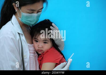 Une jolie jeune fille asiatique se sentant effrayée et nerveuse avant se faire vacciner est réconforté par son médecin qui l'est port d'un masque chirurgical avec un coup Banque D'Images