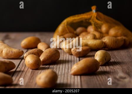 Faible profondeur de champ image sombre de petites pommes de terre ratte de forme irrégulière éparpillées sur la surface d'une table en bois d'un sac de filet à bout. Un Banque D'Images