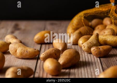 Faible profondeur de champ image sombre de petites pommes de terre ratte de forme irrégulière éparpillées sur la surface d'une table en bois d'un sac de filet à bout. Un Banque D'Images