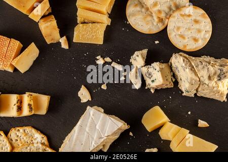 Une image de dessus d'une sélection de fromages artisanaux français, italiens et suisses âgés sur plateau de fromages noirs servis avec des craquelins. Miettes Banque D'Images