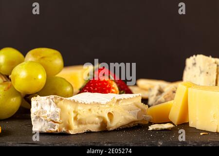 Une sélection de fromages artisanaux français, italiens et suisses de la grotte, âgés de dur et crémeux, sur plateau de fromages noirs, servis avec des crackers, des raisins et du St Banque D'Images