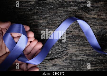 Vue de dessus du ruban bleu periwinkle tenu à la main d'un homme sur fond de bois avec espace de copie. Sensibilisation au cancer de l'estomac et de l'œsophage, troubles de l'alimentation Banque D'Images