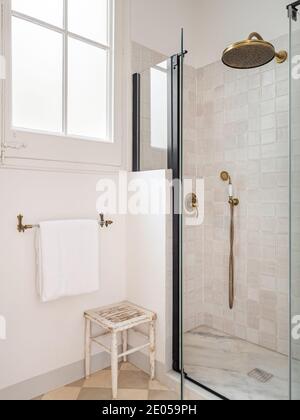 Salle de bains de couleur beige vintage avec douche, fenêtre, serviette et tabouret en bois Banque D'Images