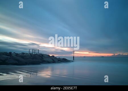 Le sable humide reflète un ciel rempli de nuages sombres et parsemés tandis que le soleil commence à s'élever au-dessus de la mer au large de la plage de Bournemouth. Banque D'Images