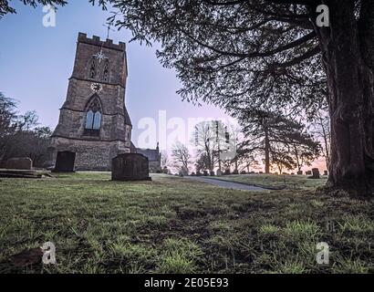 Une image solennelle de pierres tombales dans une cour d'église sur un matin de lever de soleil sombre brumeux. Banque D'Images