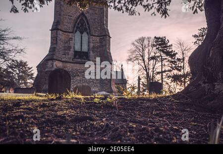 Une image solennelle de pierres tombales dans une cour d'église sur un matin de lever de soleil sombre brumeux. Banque D'Images