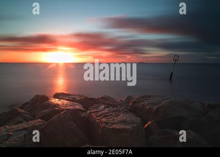 Une longue exposition capture les nuages qui s'étirent à travers le ciel tandis que le soleil se lève dans un ciel froid bleu pâle d'hiver au-dessus de Bournemouth, Dorset. Banque D'Images