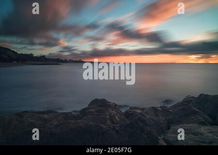 Une longue exposition capture les nuages qui s'étirent à travers le ciel tandis que le soleil se lève dans un ciel froid bleu pâle d'hiver au-dessus de Bournemouth, Dorset. Banque D'Images