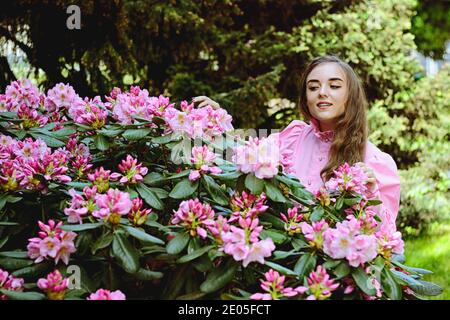 Portrait de jeune femme attrayante dans le jardin de printemps avec fleurs roses en fleur. Arrière-plan du ressort. Fête des femmes. Carte de vœux. Banque D'Images