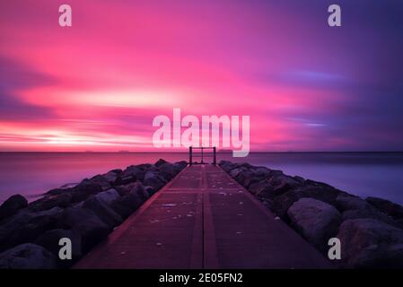 Une longue exposition transforme le mouvement des nuages en stries de couleur rose vif et pourpre tandis que le soleil se lève dans un ciel d'hiver sur la plage de Bournemouth. Banque D'Images