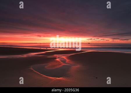 Le soleil levant remplit un ciel d'hiver de couleur sur les bassins de marée gravés dans le sable humide de la plage de Bournemouth. Banque D'Images