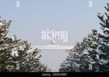 Allée d'arbres de Noël et arche avec trois grues et un globe couvert de neige en hiver, sur la place de l'indépendance en Ouzbékistan Banque D'Images