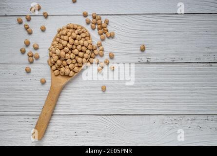 Pois chiches séchés non cuits dans une cuillère en bois sur une table en bois blanc. Un tas de légumineuses sur fond de pois chiches. Vue de dessus. Concept de nourriture végétalienne Banque D'Images